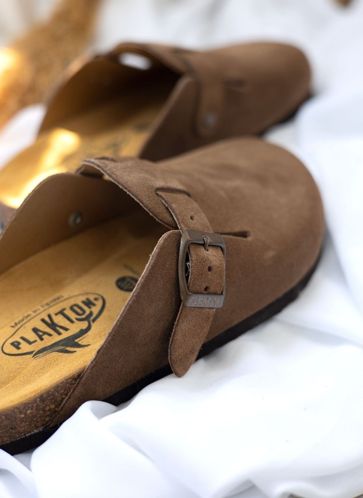 Close-up of taupe suede clog buckle strap and upper edge with cork footbed visible in warm sunlight