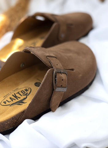 Close-up of taupe suede clog buckle strap and upper edge with cork footbed visible in warm sunlight