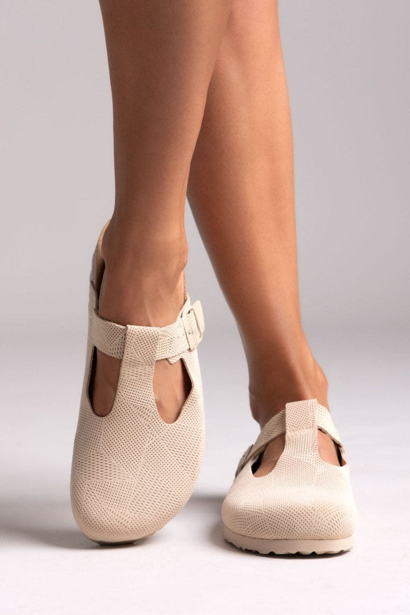 Model legs in cream suede T-strap clogs with cut-out vamp and buckle, front view on a light backdrop