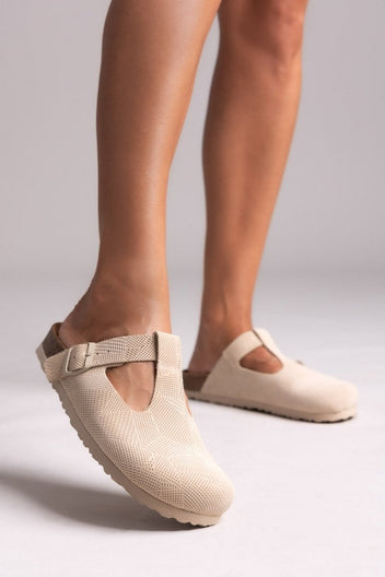 Model feet in beige suede T-strap clogs with cork footbeds, angled view on a light backdrop