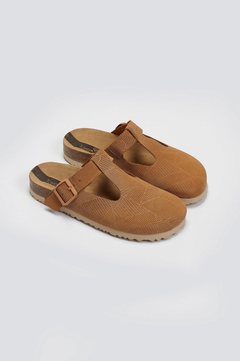 Pair of tan suede T-strap clogs with cut-out vamp and buckle, angled view on a light grey background