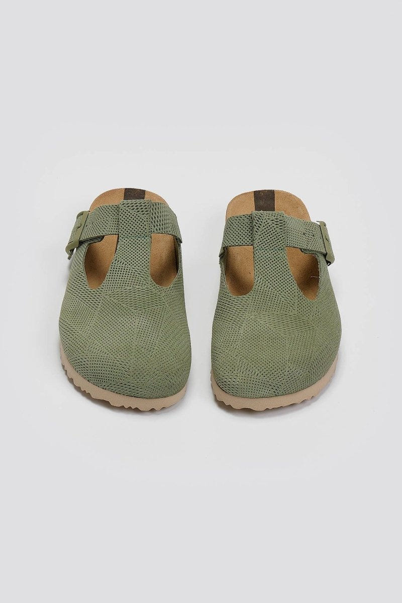 Pair of sage green suede T-strap clogs with cut-out vamp and buckle, overhead view on a light grey background