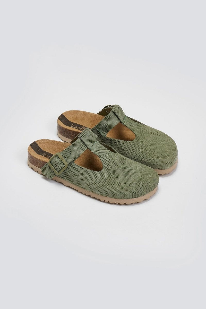 Pair of sage green suede T-strap clogs with cut-out vamp and buckle, angled view on a light grey background