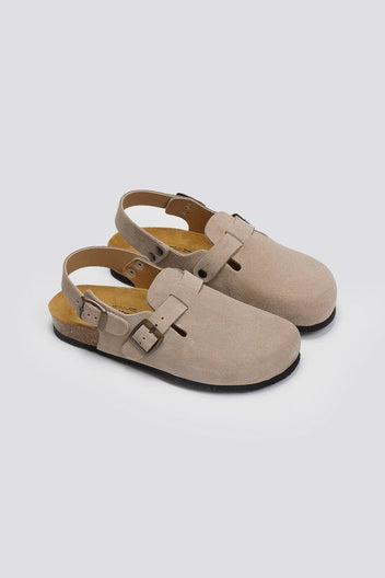Pair of taupe suede clogs with ankle strap and buckle, angled view on a light grey background