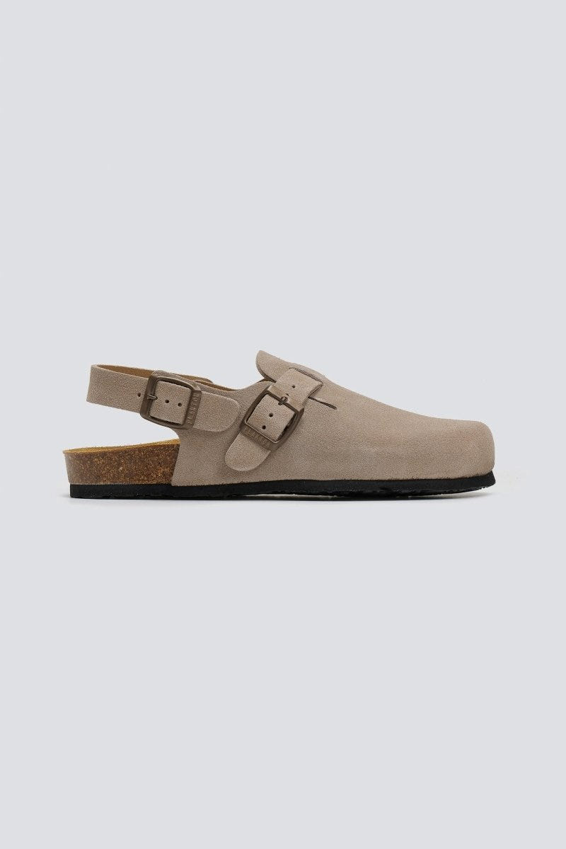 Taupe suede clog with ankle strap and buckle on a cork footbed, side view on a light grey background