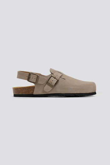 Taupe suede clog with ankle strap and buckle on a cork footbed, side view on a light grey background
