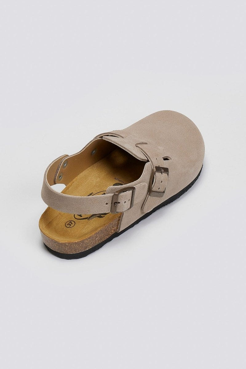 Taupe suede clog with ankle strap and buckle on a cork footbed, angled overhead view on a light grey background