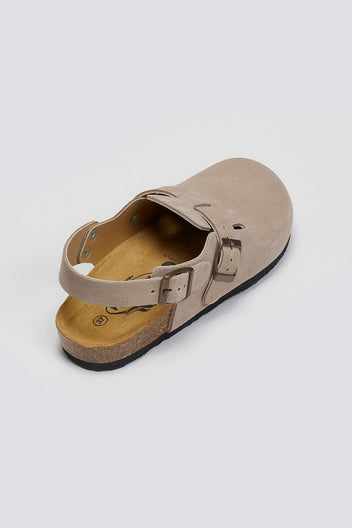 Taupe suede clog with ankle strap and buckle on a cork footbed, angled overhead view on a light grey background