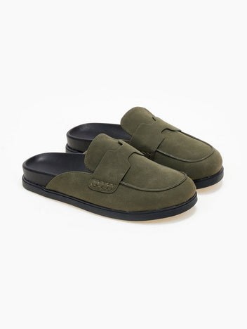 Pair of olive green suede loafer-style mules with black rubber soles, angled view on a white background