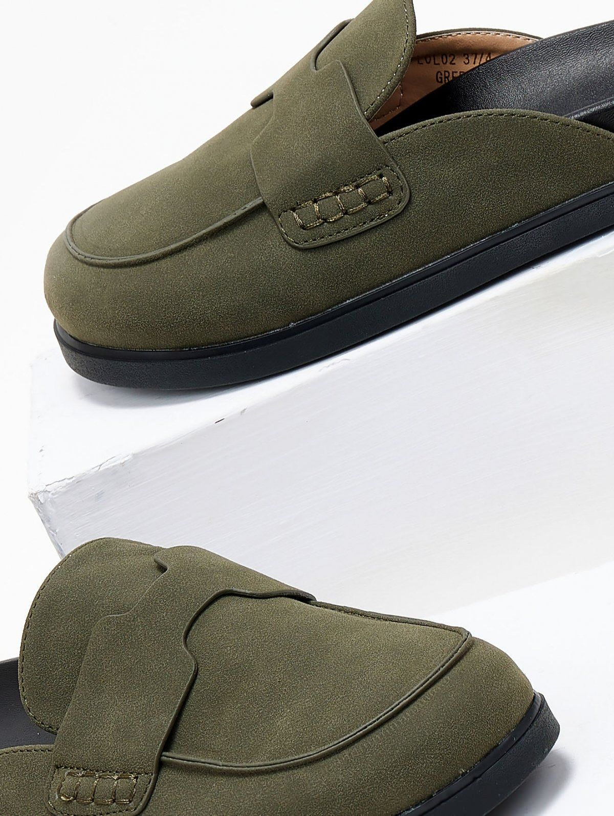 Close-up of olive green suede mule with stitched penny strap and black rubber sole on a white background