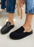 Model feet in black suede loafer-style mules with black rubber soles, worn with light blue jeans, angled view on a light backdrop