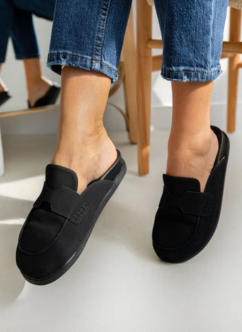 Model feet in black suede loafer-style mules with black rubber soles, worn with light blue jeans, angled view on a light backdrop