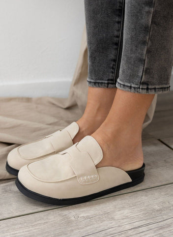 Model feet in cream suede loafer-style mules with black rubber soles, worn with dark jeans, front view on a light backdrop