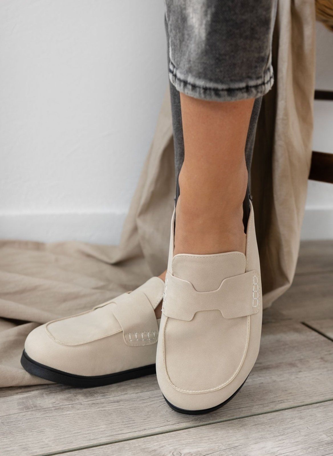 Model feet in cream suede loafer-style mules with black rubber soles, worn with grey trousers, angled view on a light backdrop