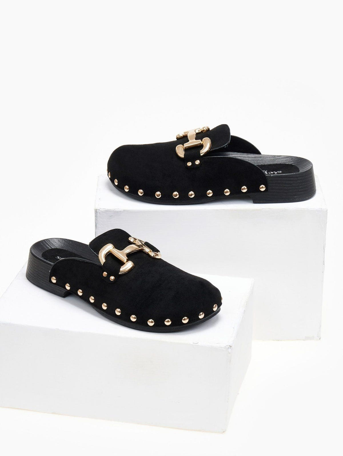 Black suede clog with gold horsebit buckle and gold studs, angled view on a white display block