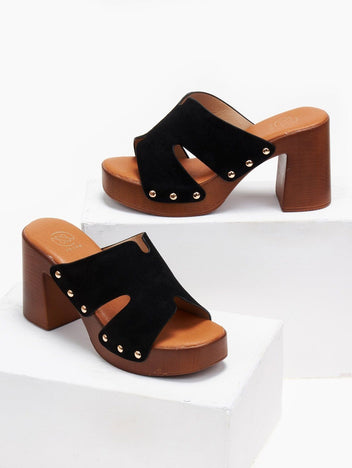 Pair of black suede block heel slides with gold studs and tan platform, angled view on a white display block