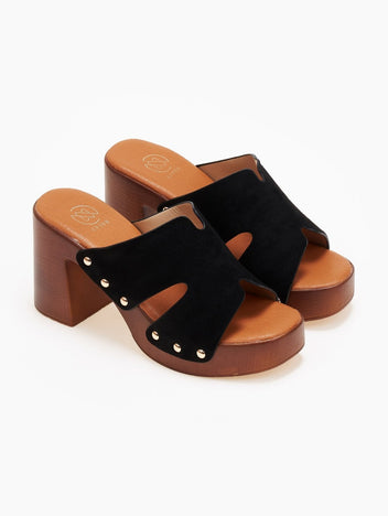 Pair of black suede block heel slides with cut-out straps, gold studs and tan wooden-look platform, angled view on light grey