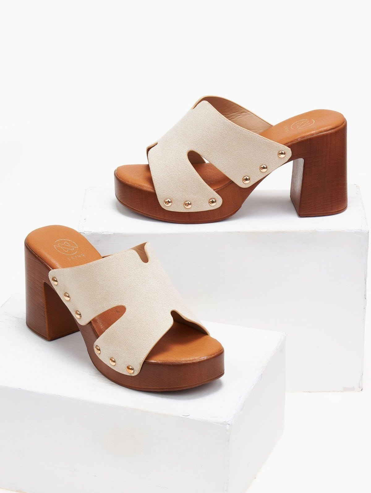 Pair of cream suede block heel slides with tan wooden-look platform and cut-out straps, angled view on a white background