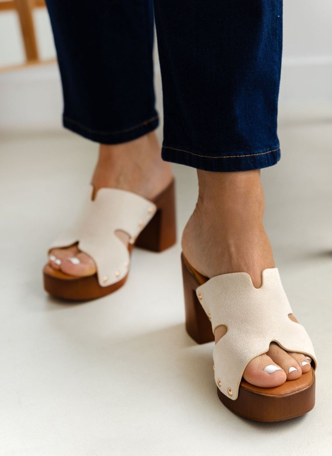 Model feet in cream suede block heel slides with tan wooden-look platform, worn with dark jeans, front view on a light backdrop