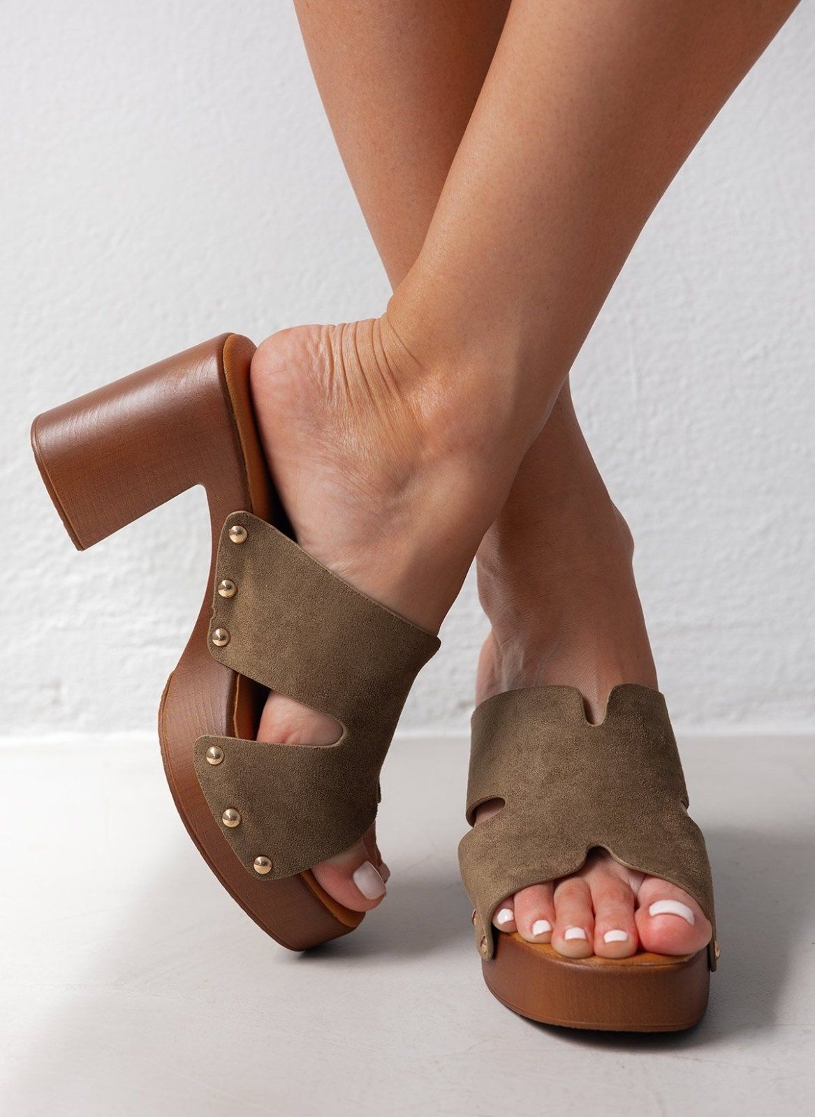 Model feet in olive suede block heel slides with cut-out straps and wooden-look platform, angled view on a light backdrop