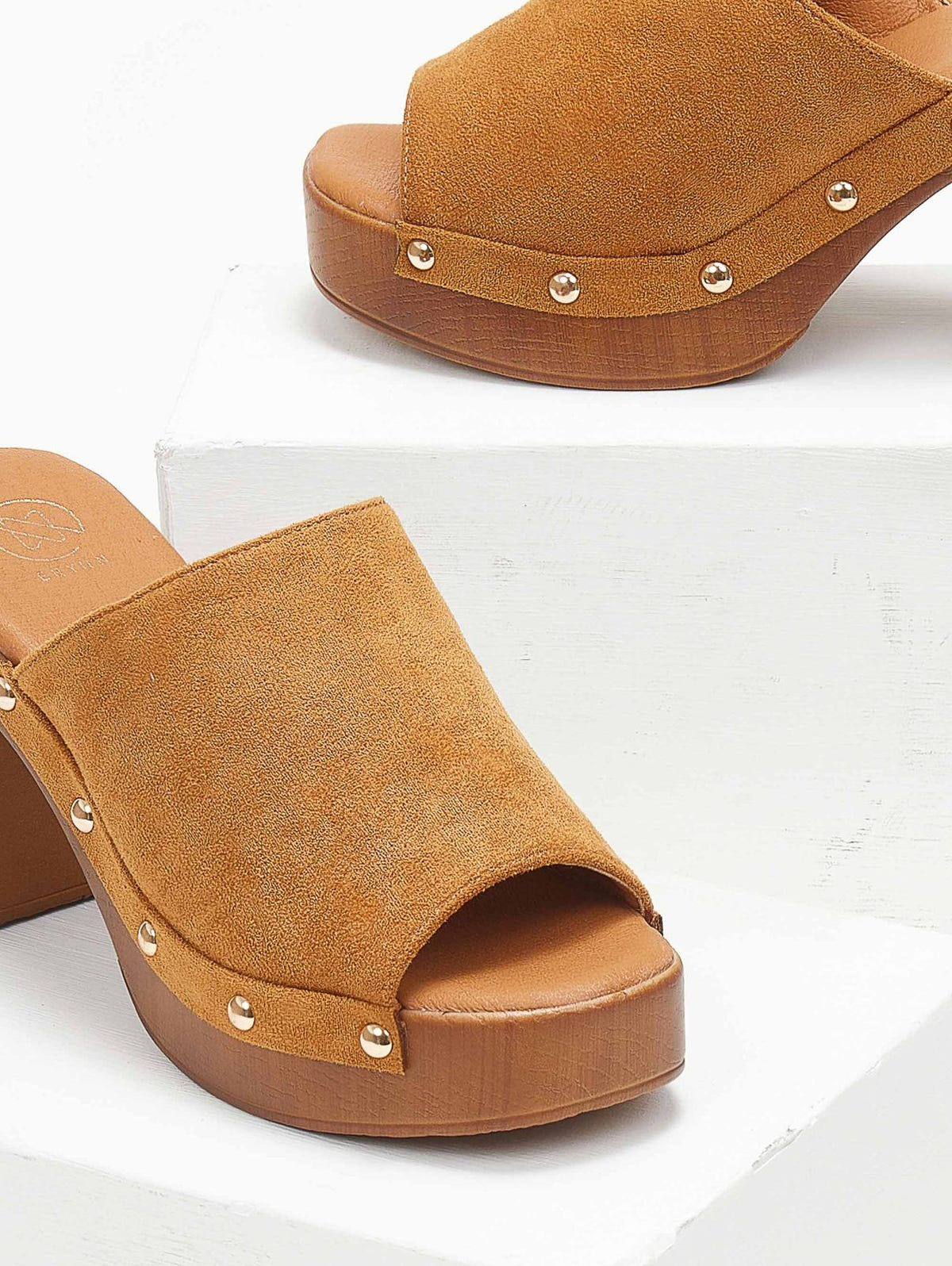 Close-up of tan suede block heel slide with gold studs and wooden-look platform, angled view on a white display block