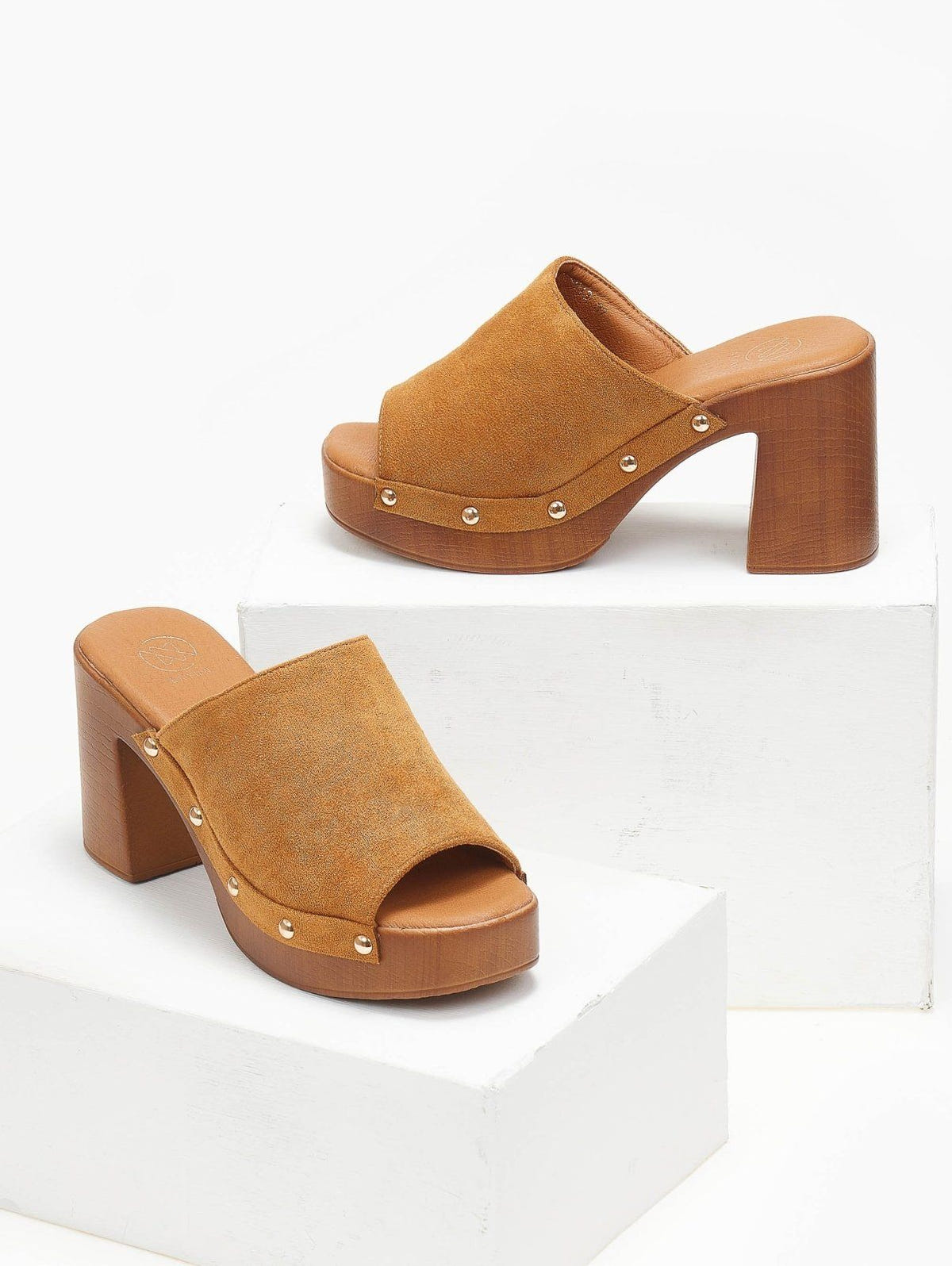 Pair of olive suede block heel slides with gold studs and wooden-look platform, angled view on a white display block