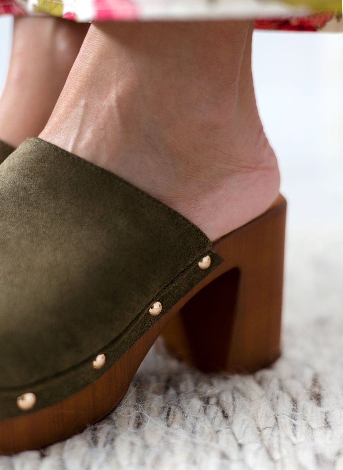 Model feet in olive suede block heel slides with wooden-look platform and gold studs, close view on a light background