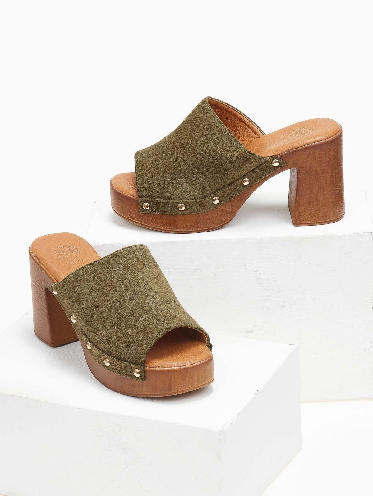 Pair of olive suede block heel slides with wooden-look platform and gold studs, angled view on a white display block