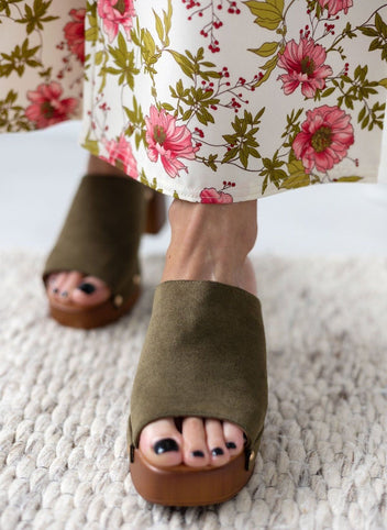 Model feet in olive suede block heel slides with wooden-look platform, worn with floral print trousers, front view