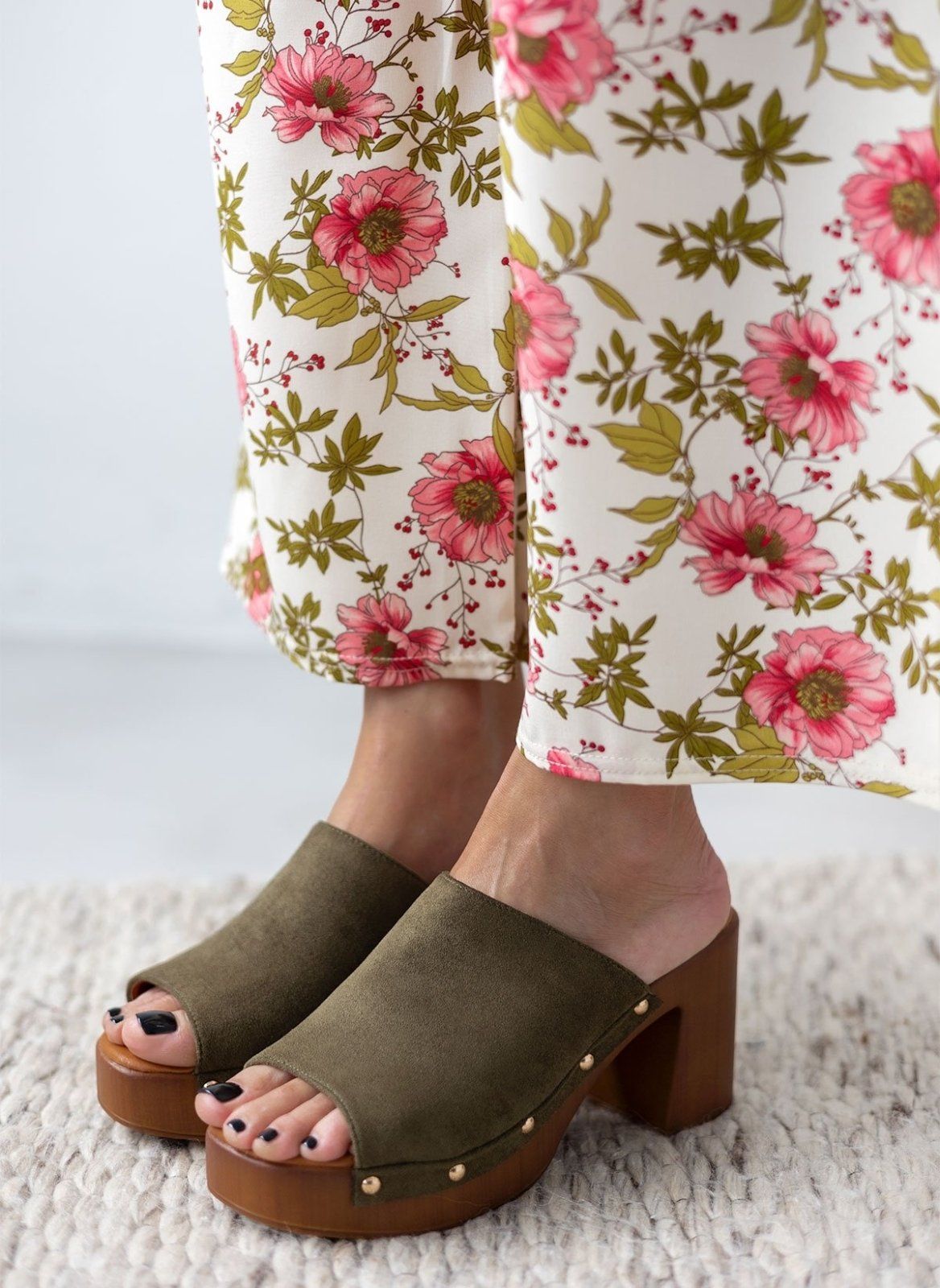 Model feet in olive suede block heel slides with wooden-look platform, worn with floral print trousers, front view
