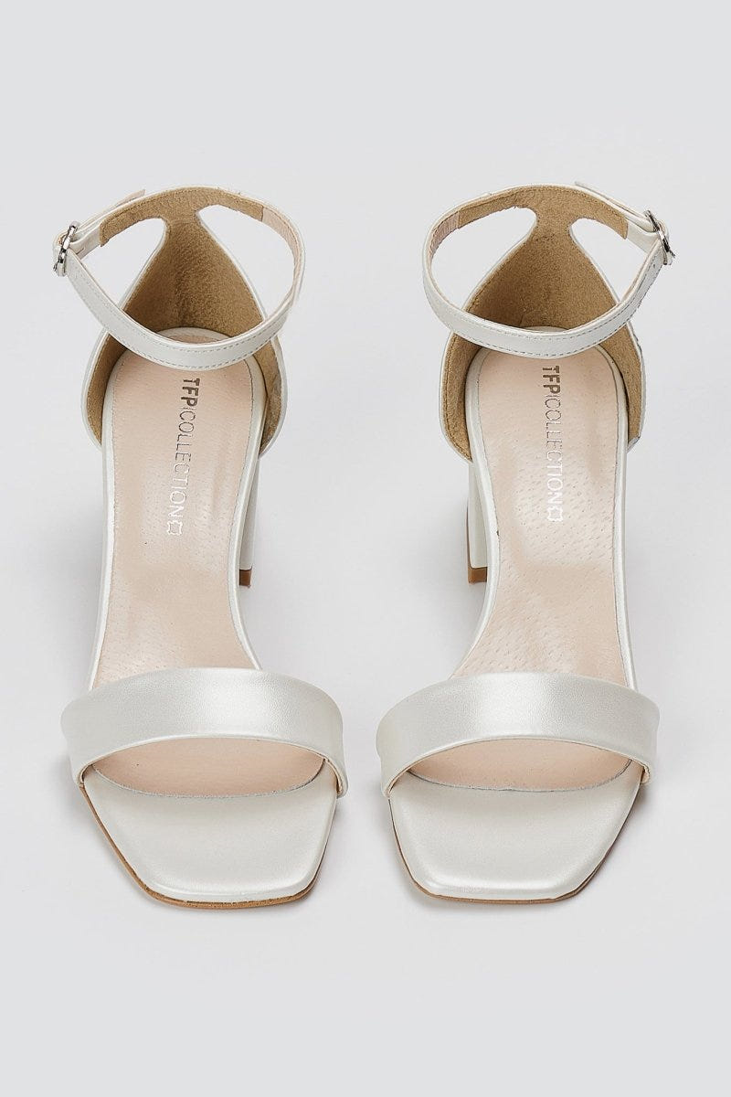 Pair of metallic silver leather block heel sandals with ankle straps and square open toes, overhead view on light grey