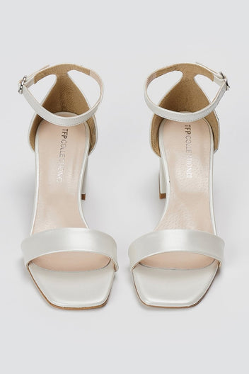 Pair of metallic silver leather block heel sandals with ankle straps and square open toes, overhead view on light grey