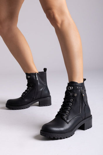 Model legs in black leather lace-up ankle boots with side zips and chunky lug soles, angled view on a light grey background