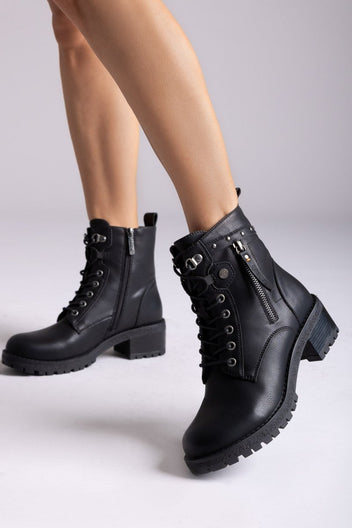 Model legs in black leather lace-up ankle boots with chunky lug soles and side zip, angled view on a light backdrop