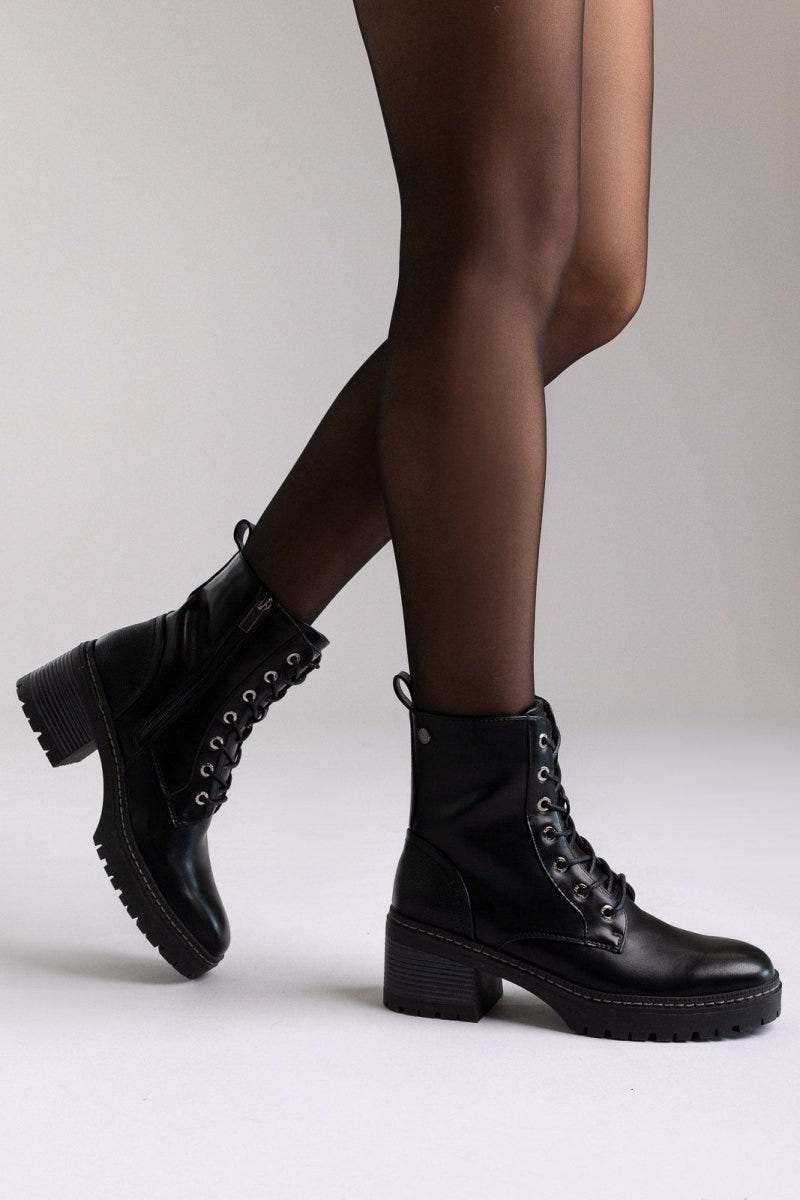 Model legs in black leather lace-up ankle boots with chunky block heels, angled view on a light background