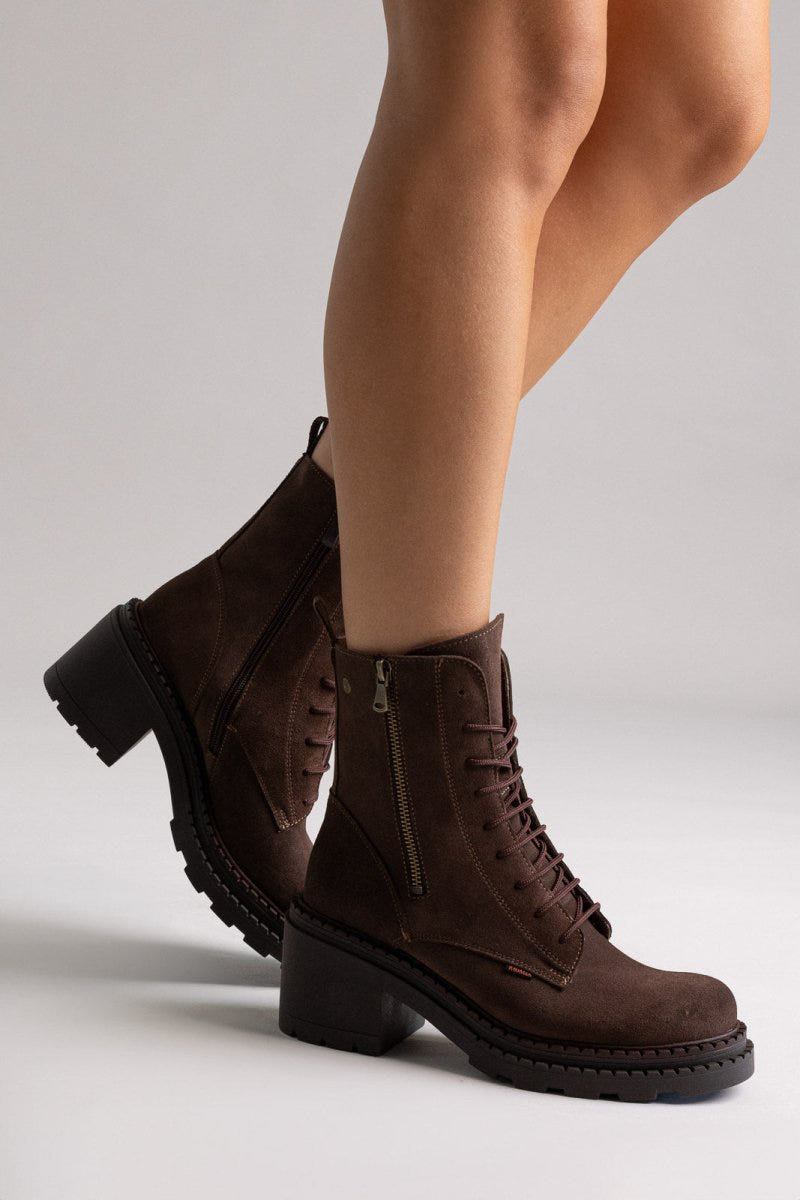 Model legs in dark brown suede lace up boots with block heel and chunky sole, angled view on light grey background