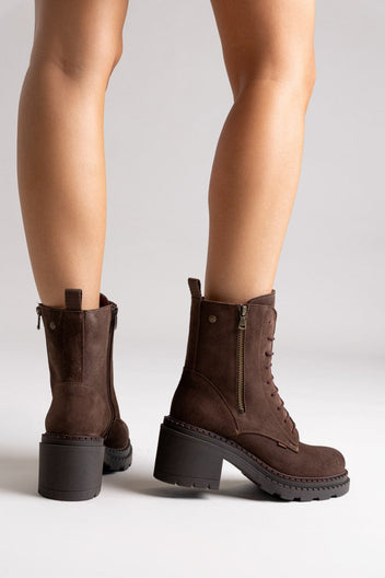 Model legs in dark brown suede lace up boots with block heel and chunky sole, angled view on light grey background
