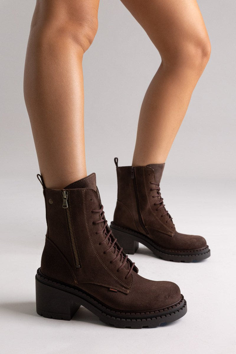 Model legs in dark brown suede lace up boots with block heel and chunky sole, angled view on light grey background