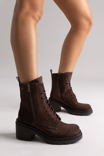 Model legs in dark brown suede lace up boots with block heel and chunky sole, angled view on light grey background