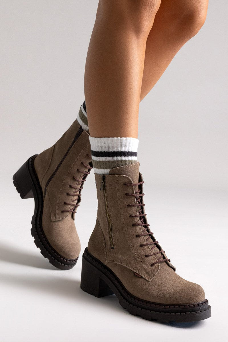Model legs in taupe suede lace up boots with block heel and striped socks, angled view on light grey background