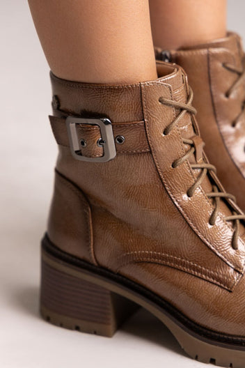 Close-up of brown leather lace-up ankle boot with buckle strap and block heel, angled view on a light backdrop