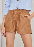 Caramel faux leather shorts with elasticated waist and two large patch pockets on the front, worn on model, front view