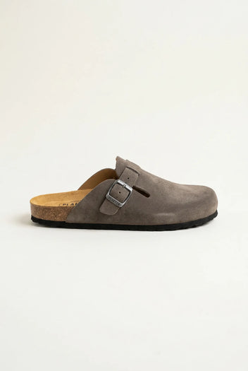 Side view of a taupe suede buckle clog with a cork footbed, black rubber sole and a slotted strap detail