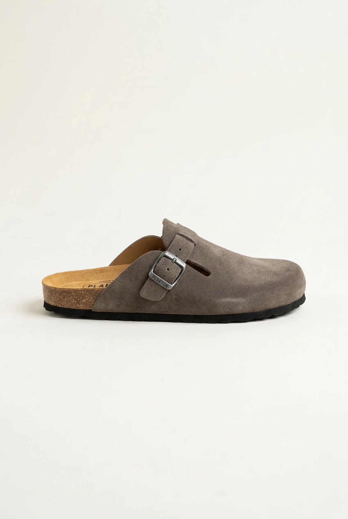 Side view of a taupe suede buckle clog with a cork footbed, black rubber sole and a slotted strap detail