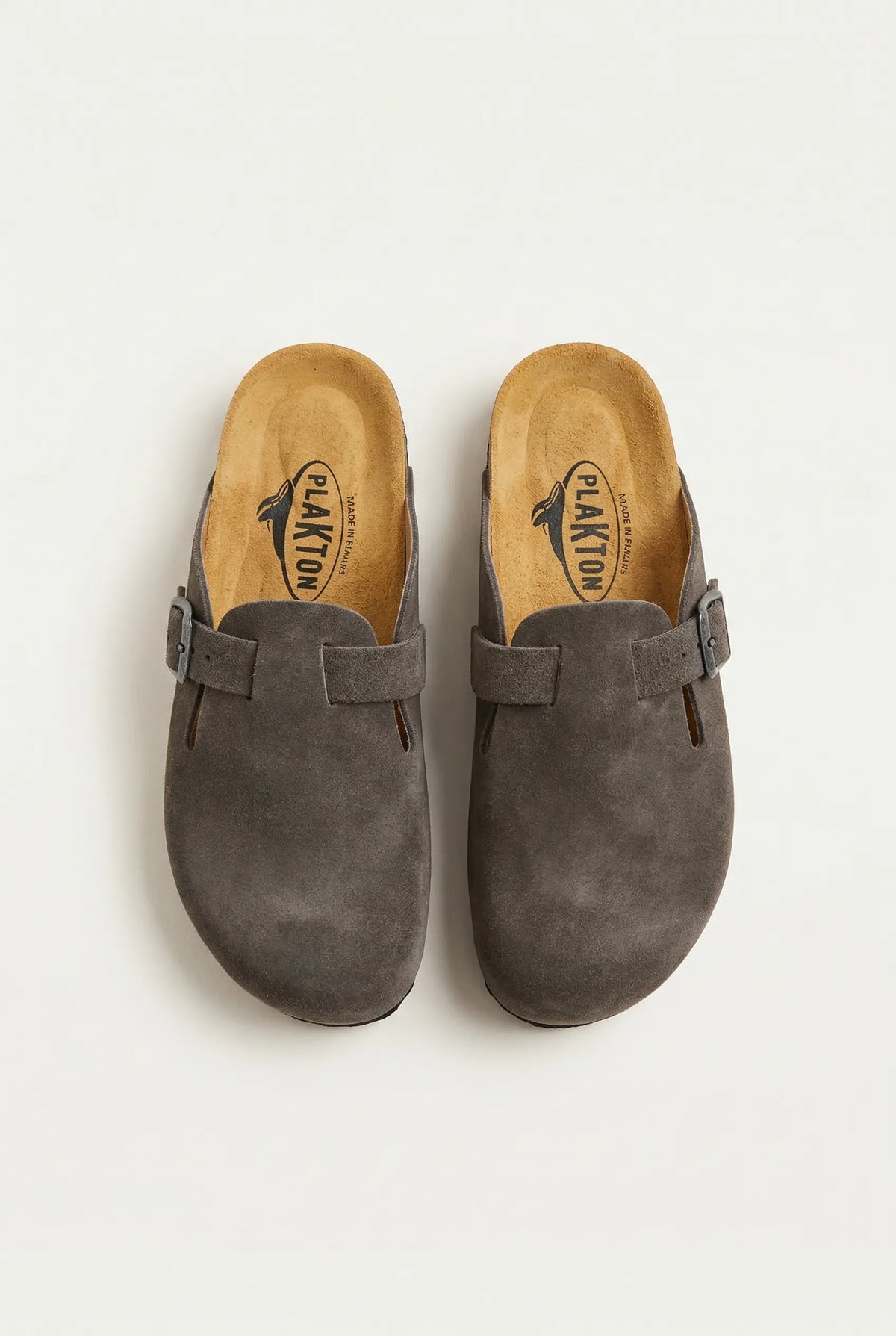 Top-down view of a pair of grey suede clogs with buckle straps and tan cork footbeds with a printed whale logo