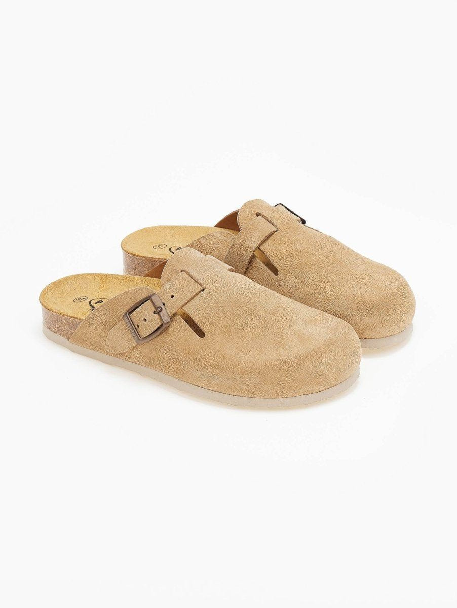 Pair of beige suede clogs with buckle straps and cork footbeds seen at an angle on white surface