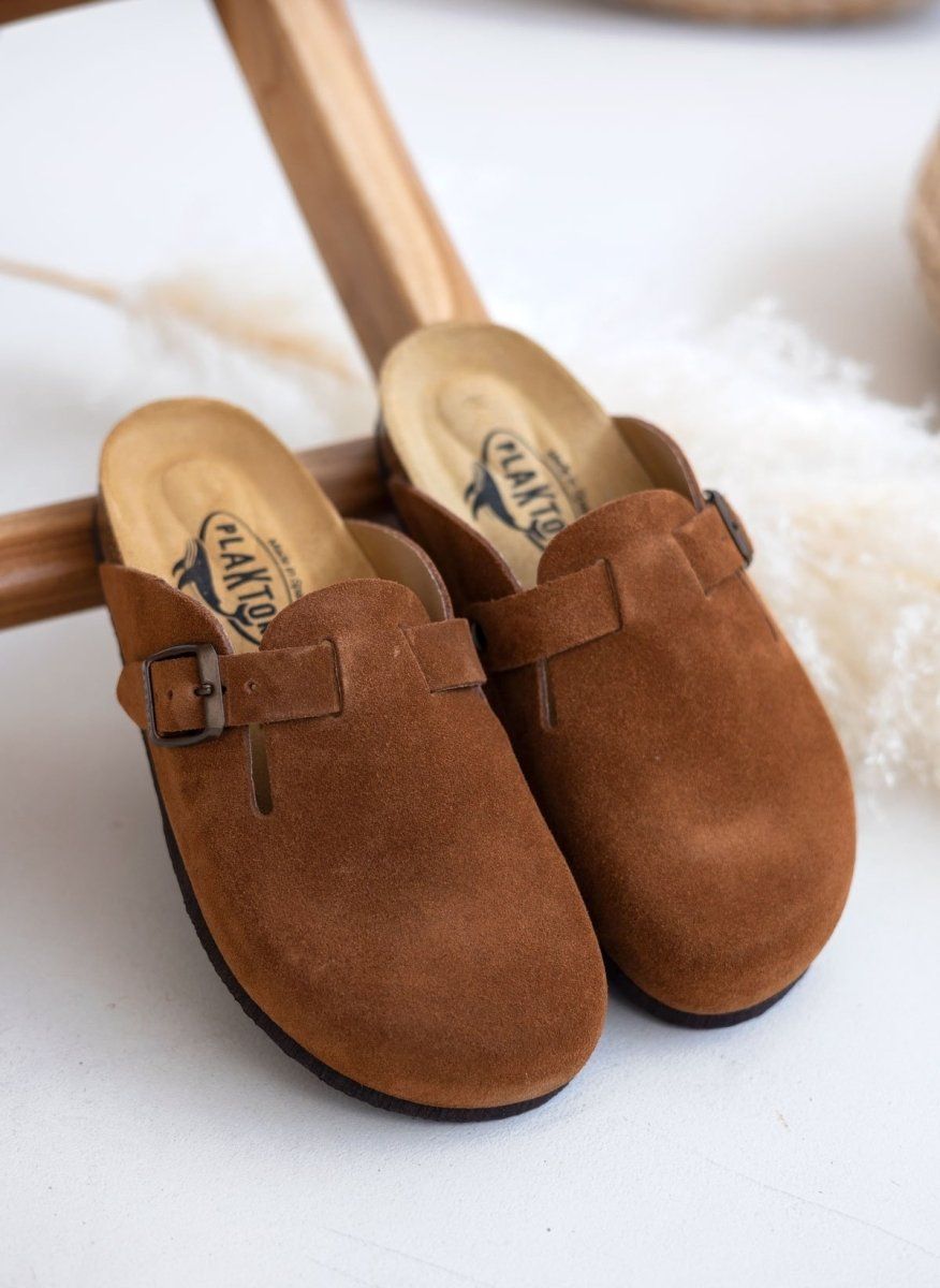 Pair of brown suede clogs with buckle strap and cork footbeds, angled view on a light background