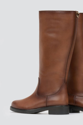 Cognac brown leather knee-high riding boot with flat sole and side zip, angled view on a light grey background
