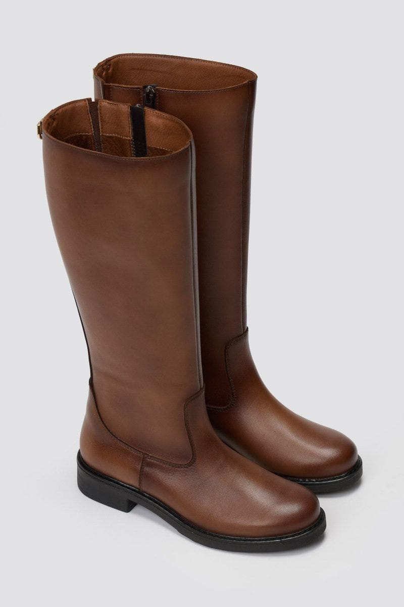 Pair of cognac brown leather knee-high riding boots with flat soles, angled view on a light grey background