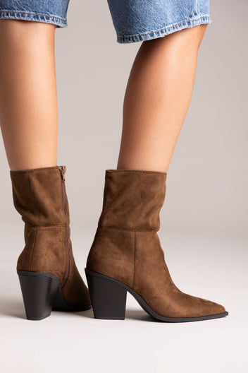 Model legs in dark brown suede pointed ankle boots with block heels and slouched shafts, angled view on a light backdrop